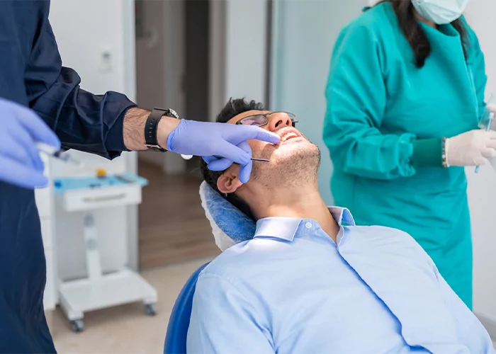 doctor pointing at patient teeth with an assistant in background