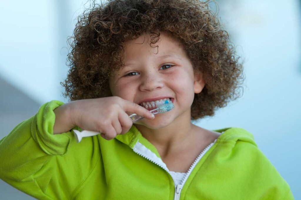 a child brushing their teeth smiling at the camera