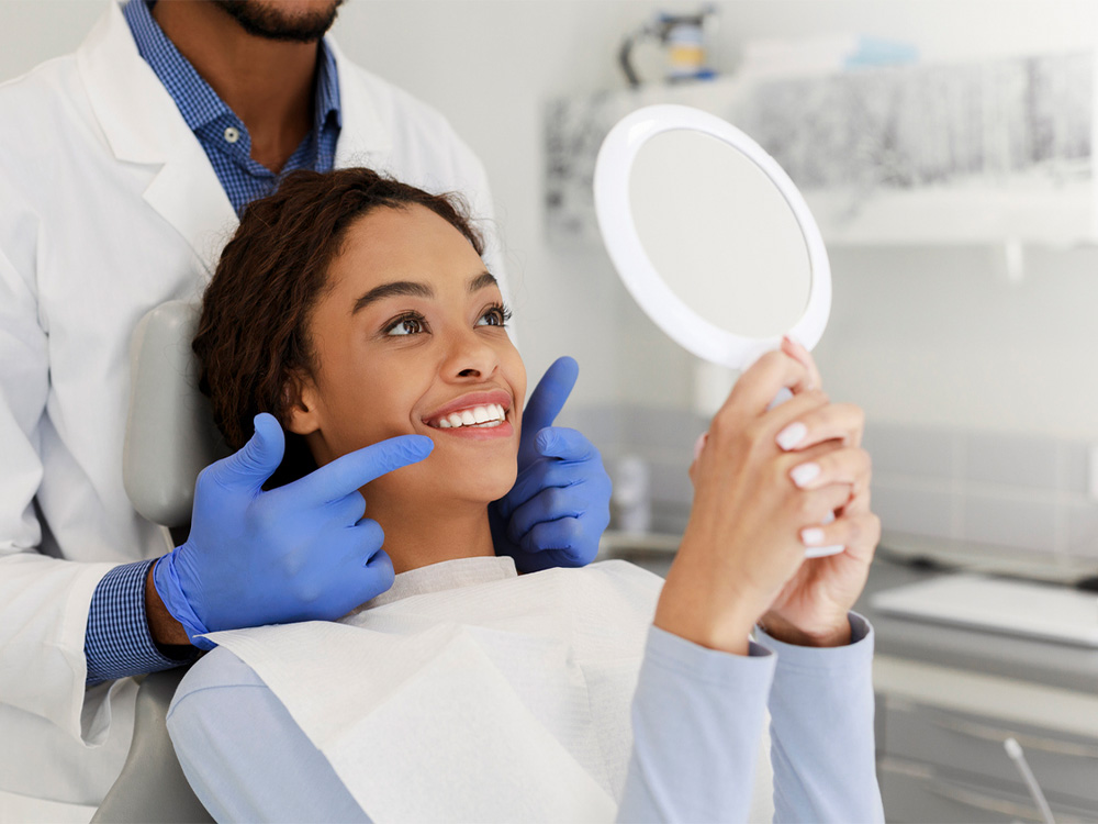 patient smiling into a mirror with the doctor pointing to her teeth behind her